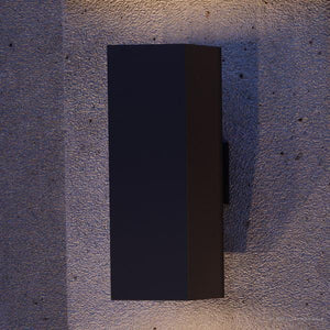 An UHP1113 Minimalist Outdoor Wall Light, 18"H x 6"W, Midnight Black Finish, Madrid Collection by Urban Ambiance beautifully illuminating a concrete wall.
