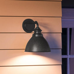 An UHP1174 Hammered Outdoor Wall Light, 9-3/4" x 8", Midnight Black Finish, Firenze Collection by Urban Ambiance on the side of a house.
