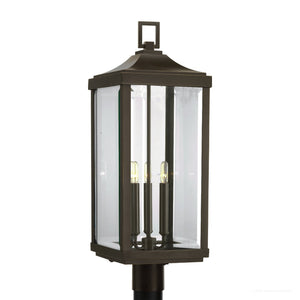 The UHP1190 Colonial Outdoor Post / Pier Light from the Calderdale Collection by Urban Ambiance features a rectangular design with an Olde Bronze finish, clear beveled glass panels, and three vertical candle-style bulbs inside. It measures 26-7/8″ x 9-1/2″.