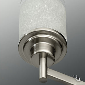 Close-up of a modern wall sconce with a brushed nickel finish and a cylindrical, textured white lampshade—designed to complement the UHP2017 Contemporary Chandelier from Urban Ambiance’s Cupertino Collection—set against a gray background.