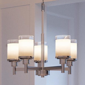 The Urban Ambiance UHP2017 Contemporary Chandelier from the Cupertino Collection features five cylindrical frosted glass shades and a brushed nickel frame, elegantly suspended from the ceiling in a neutral-toned room.