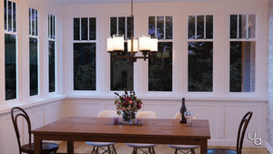 A unique lighting fixture, the UHP2018 Contemporary Chandelier from the Cupertino Collection by Urban Ambiance, illuminates a dining room with an Olde Bronze Finish wooden table and chairs.