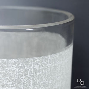 Close-up of the UHP2019 Contemporary Chandelier from Urban Ambiance’s Cupertino Collection, showcasing its cylindrical glass form with a frosted textured lower half and clear upper rim, all highlighted by a refined brushed nickel finish. The composition against a dark background evokes the sleek lines and understated elegance characteristic of modern chandelier design.