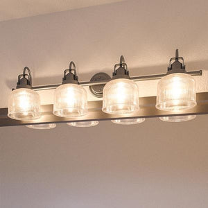 A contemporary wall-mounted fixture from the Harlow Collection, the UHP2048 Luxe Industrial Bath Fixture by Urban Ambiance features five illuminated prismatic glass shades and an aged nickel finish, installed above a mirror.