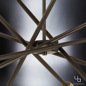 Close-up of intersecting bronze metal rods from the UHP2072 Modern Industrial Chandelier (10-1/2″H x 22-5/8″W, Olde Bronze Finish, Miami Collection) by Urban Ambiance, reminiscent of a Sputnik chandelier, set against a gradient black and white background with a small “ua” logo in the lower right corner.