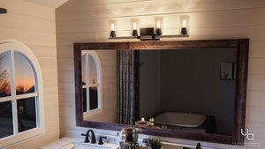 Modern bathroom featuring a large framed mirror, a four-bulb light fixture above, a white vanity with the Urban Ambiance UHP2082 Vintage Bath Fixture from the Darlington Collection (8″H x 32-1/4″W, Olde Bronze finish), and an arched window showcasing the sunset outside.