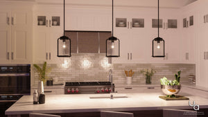 Modern kitchen with white cabinets, three Urban Ambiance UHP2111 Nautical Pendant Lights from the Carlsbad Collection in Olde Bronze finish featuring seeded glass shades, a central island with a sink, and a bowl of vegetables on the countertop.