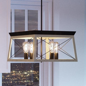 The UHP2123 Luxe Industrial Chandelier by Urban Ambiance features a geometric, open-cage metal frame in a charcoal finish and exposed bulbs, hanging indoors near a window overlooking a nighttime cityscape. Part of the Berkeley Collection, it measures 12″H x 20″W.