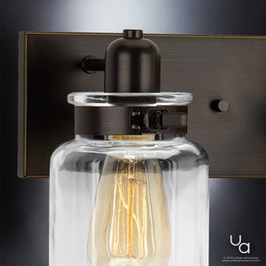 Close-up of the Urban Ambiance UHP2143 Modern Farmhouse Industrial Bath Fixture from the Bridgeport Collection, featuring an 8-5/8″ high by 21-5/8″ wide design with a clear glass shade reminiscent of jar lighting, exposed filament bulb, and an Olde Bronze finish for a vintage-inspired bathroom light look.