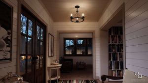A hallway with white shiplap walls, a striped rug, bookshelves, and the Urban Ambiance UHP2241 Luxe Industrial Ceiling Fixture from the Nashville Collection—measuring 15 inches high by nearly 20 inches wide and finished in charcoal—creates an industrial chic atmosphere with its vintage-style bulbs as it leads to a sitting room where windows reveal dusk-lit trees outside.
