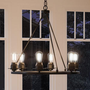 The UHP2243 Luxe Industrial Chandelier from Urban Ambiance’s Nashville Collection, featuring a 27-1/2 inch height and a 28 inch width with a charcoal finish, hangs in front of large windows at dusk, its six exposed bulbs filling the room with warm light.
