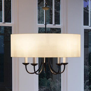 The Urban Ambiance UHP2281 Transitional Chandelier from the Aurora Collection features an Olde Bronze finish and hangs elegantly in front of tall windows, its sophisticated design highlighted by black metal arms, four candle-style bulbs, and a large white fabric drum shade.