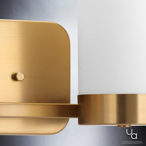 Close-up of the Urban Ambiance UHP2291 Contemporary Bathroom Vanity Light from the Madison Collection, featuring a brushed bronze finish and cylindrical frosted glass shades against a gray background, showcasing subtle influences from open-frame lighting for an added touch of contemporary elegance.