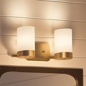 The Urban Ambiance UHP2291 Contemporary Bathroom Vanity Light from the Madison Collection, featuring a brushed bronze finish and two frosted cylindrical glass shades, is mounted on a white paneled wall above a mirror.