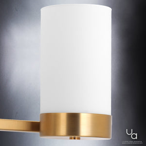 Featuring the UHP2293 Contemporary Bathroom Vanity Light from Urban Ambiance’s Madison Collection, this elegant fixture showcases a sleek cylindrical design in a brushed bronze finish. Its refined look pairs effortlessly with a crystal indoor chandelier, infusing any space with sophisticated charm against a modern gray backdrop.