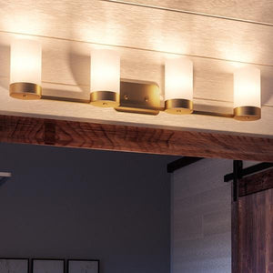 The Urban Ambiance UHP2295 Contemporary Bathroom Vanity Light from the Madison Collection, measuring 7.5 inches high by 34.5 inches wide and featuring a brushed bronze finish, is installed on a light-colored ceiling above a doorway with wood trim. The fixture has four cylindrical frosted glass shades, offering a modern touch to the space.