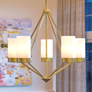 The Urban Ambiance UHP2301 Contemporary Chandelier from the Madison Collection showcases a brushed bronze finish and six cylindrical white lampshades, adding a modern touch to any room adorned with a large abstract painting and beige curtains.