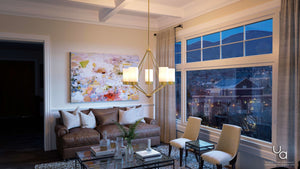 A modern living room with a brown leather sofa, abstract wall art, glass coffee tables, and a window revealing a cityscape and mountains at dusk. The space is elegantly illuminated by the Urban Ambiance UHP2301 Contemporary Chandelier from the Madison Collection, featuring etched glass shades and a brushed bronze finish (23″H x 27.375″W).