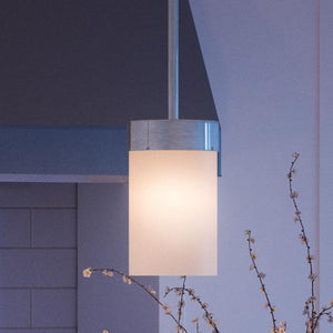 The Urban Ambiance UHP2307 Transitional Pendant Light from the Madison Collection, measuring 7″ x 5-1/8″ with a polished chrome finish and a frosted, etched white glass shade, hangs from the ceiling near a tiled wall and a branch adorned with small buds.