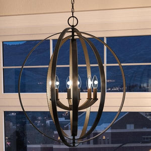 The UHP2330 Luxe Industrial Chandelier from the Arezzo Collection by Urban Ambiance, measuring 30″ high by 27-3/4″ wide and finished in Olde Bronze, with five exposed bulbs, hangs in front of a window overlooking a nighttime cityscape.