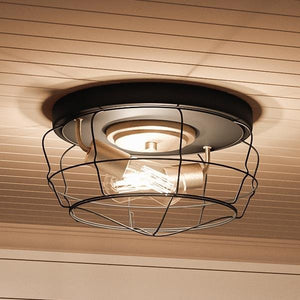The UHP2423 Vintage Ceiling Fixture from the Syracuse Collection by Urban Ambiance features a round charcoal-finished base and an exposed bulb, encased in an open black wire cage design. Measuring 6.75″ high by 14″ wide, this modern industrial ceiling light is mounted on a white paneled ceiling, adding a touch of vintage industrial style to any space.