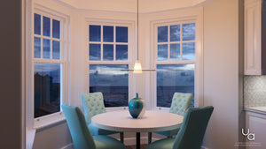 A round white table with a blue vase, four teal chairs, and large bay windows revealing an evening ocean view sits beneath the Urban Ambiance UHP2431 Contemporary Pendant Light from the Honolulu Collection—a 7.5″H x 20″W brushed nickel fixture that softly illuminates the space.