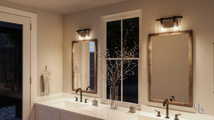 A bathroom featuring double sinks and two mirrors is illuminated by the Urban Ambiance UHP2452 Modern Farmhouse Modern Bath Fixture from the Bristol Collection, finished in Olde Bronze and mounted on the wall. A vase with branches decorates the counter, while a towel hangs on the left wall near the door.
