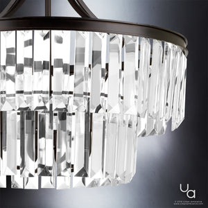 Close-up of the Urban Ambiance UHP2462 Traditional Chandelier from the Lille Collection, showcasing two tiers of clear rectangular crystal prisms reminiscent of prismatic glass, suspended from a dark Olde Bronze-finished metal frame against a softly gradient background. The chandelier measures 23-7/8″ high by 22-1/4″ wide.