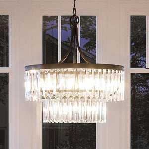 The Urban Ambiance UHP2462 Traditional Chandelier from the Lille Collection features a two-tiered design with a handcrafted metal frame in an Olde Bronze finish; at 23-7/8″ high and 22-1/4″ wide, this striking fixture glows warmly as it hangs before tall windows at dusk.