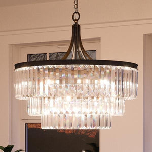 The UHP2464 Traditional Chandelier from Urban Ambiance’s Lille Collection features three tiers of vertical prismatic glass prisms gracefully suspended from a black metal frame with an elegant Olde Bronze finish, creating a striking statement piece reminiscent of classic sophistication. Measuring 29-1/4″ high by 28″ wide, this sparkling chandelier illuminates any room with timeless style.