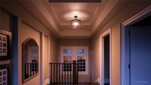 A hallway with beige walls features the Urban Ambiance UHP2467 Cosmopolitan Ceiling Light from the Lille Collection, measuring 15-1/2″ x 13-1/8″ and finished in Olde Bronze, with prismatic glass. Framed photos and a mirror accent the space as it leads to a window overlooking an evening sky, with doors open on both sides.