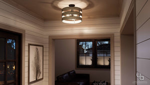 A hallway with white shiplap walls, framed art, a window, and a partial view of a dark sofa in an adjacent room features the Urban Ambiance Adelaide Collection UHP2470 Modern Farmhouse Flush-Mount Ceiling Fixture (13-1/2″H x 17″W) in a charcoal finish.