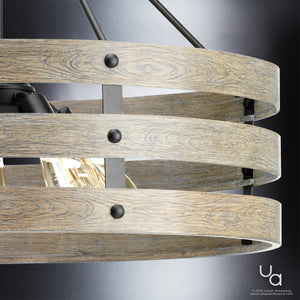 Close-up of the UHP2478 Modern Farmhouse Chandelier from the Adelaide Collection by Urban Ambiance, featuring three wood-finished metal rings and exposed bulbs in a striking charcoal finish. This 22-3/4″ high by 27-3/4″ wide open cage pendant light is mounted with black hardware against a dark gradient background, seamlessly blending rustic and contemporary design elements for a modern statement piece.