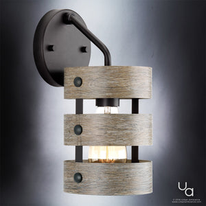 Experience the Urban Ambiance UHP2480 Modern Farmhouse Bath / Wall Light from the Adelaide Collection—measuring 12″H x 6″W with a charcoal finish, this fixture showcases a bulb surrounded by three wood-textured horizontal bands and a sleek black circular base, photographed against a gradient backdrop. Ideal as a farmhouse bath fixture or rustic bathroom light.