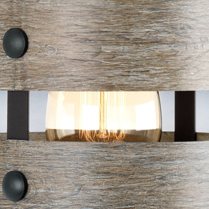 A close-up view of the Urban Ambiance UHP2480 Modern Farmhouse Bath / Wall Light from the Adelaide Collection shows its prominent light bulb with visible filaments, partially framed by two wooden slats accented with round black metal details—an ideal touch for a rustic bathroom or farmhouse-style bath, measuring 12″ high by 6″ wide in a charcoal finish.