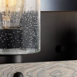 Close-up of the UHP2486 Modern Farmhouse Bath Fixture from Urban Ambiance’s Adelaide Collection, featuring a clear bubbled glass shade with a visible bulb and mounted on a charcoal-finished dark metal frame—an ideal accent for modern farmhouse decor.