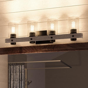A four-light Urban Ambiance UHP2486 Modern Farmhouse Bath Fixture from the Adelaide Collection, featuring clear glass shades and a charcoal finish, is mounted on a wooden plank and paired with a modern farmhouse ceiling fan, both attached to a white shiplap ceiling above a mirror and patterned curtains.