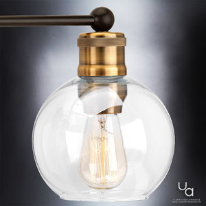 The UHP2504 Vintage Industrial Bath Fixture from Urban Ambiance’s Belfast Collection features a combination of brass and glass, showcased in an Olde Bronze finish. Measuring 10-7/8″ high by 33-1/2″ wide, this wall sconce displays a visible filament bulb on a dark rod and is set against a neutral background. Blending classic appeal with modern elegance, this vintage-inspired lighting piece adds a timeless touch to any space.
