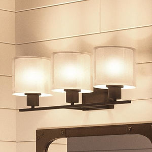 Three Cosmopolitan bathroom vanity lights from the Tacoma Collection by Urban Ambiance are mounted on a tiled wall, each featuring a cylindrical white Mylar shade and a sophisticated Olde Bronze finish for an elegant, contemporary aesthetic.
