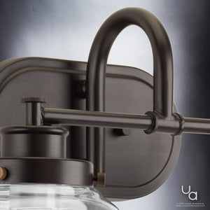 Close-up of the UHP2537 Luxe Industrial Bathroom Vanity Light from the Nottingham Collection by Urban Ambiance, featuring an 11.25″H x 16.25″W wall-mounted design with an Olde Bronze metal frame, cylindrical glass shade, and prominent vintage-style metal fittings set against a gradient background.