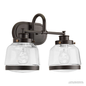 The Urban Ambiance UHP2537 Luxe Industrial Bathroom Vanity Light from the Nottingham Collection showcases a double wall sconce design with two clear glass shades and a metal fixture in an Olde Bronze finish, each exposing a standard bulb. Inspired by classic schoolhouse bath lights, vintage metal fittings add timeless appeal to this 11.25″ high by 16.25″ wide piece.