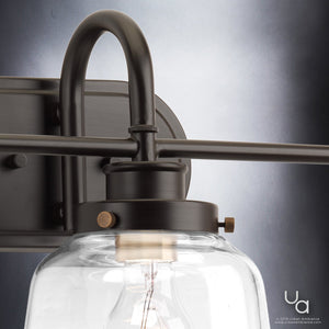 Close-up view of the Urban Ambiance UHP2539 Luxe Industrial Bathroom Vanity Light from the Nottingham Collection, measuring 11.25″ high by 26″ wide, featuring a clear glass shade, metal mounting plate in an Olde Bronze finish, and exposed bulb against a gradient background—blending the classic charm of schoolhouse globe lighting with sleek contemporary design.
