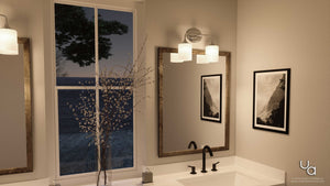 A modern bathroom features a large mirror, a black faucet, framed photos, a vase with branches, and the Urban Ambiance UHP2570 Contemporary Bathroom Vanity Light from the Coventry Collection (11.125″H x 14.5″W, Polished Chrome Finish), with a window revealing an evening outdoor scene.