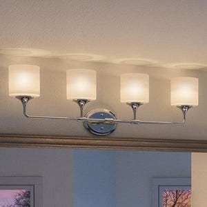 Four UHP2572 Contemporary Bathroom Vanity Lights from the Coventry Collection by Urban Ambiance, featuring frosted etched opal glass shades and a polished chrome finish, are mounted on a single horizontal metal bar above two windows for a sleek contemporary look. Each fixture measures 11.125″H x 33.25″W, adding modern elegance to the bathroom space.