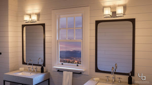 Modern bathroom with two sinks and two mirrors, each accented by Urban Ambiance’s UHP2601 Transitional Bathroom Vanity Light from the Modena Collection in a polished chrome finish; a window in between reveals a cityscape framed by mountains at sunset.