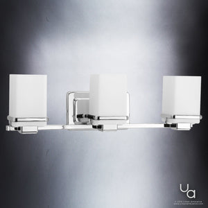The Urban Ambiance UHP2603 Transitional Bathroom Vanity Light from the Modena Collection features a sleek polished chrome finish and three square frosted glass shades, measuring 6.5″ high by 22.125″ wide. Perfect as a contemporary bath fixture mounted on a gray wall, this modern design seamlessly blends style and functionality for elegant bathroom lighting.