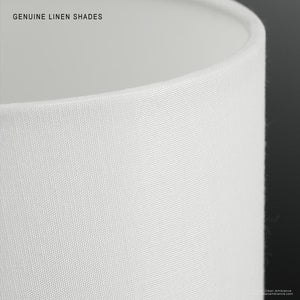 A close-up of the UHP2632 Cosmopolitan Drum Chandelier from Urban Ambiance’s Oxford Collection showcases its white linen shade with a smooth texture, set against a dark background. Subtle marble accents complement the Palladian Gold finish, and text in the image reads “GENUINE LINEN SHADES.”.
