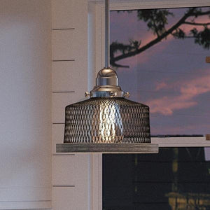 The UHP2730 Vintage Pendant Light from Urban Ambiance’s Eugene Collection features a brushed nickel finish and hangs indoors near a window at sunset. With its distinctive wire mesh shade, this 7-inch by 8-inch industrial pendant light is turned on, casting a warm glow and infusing the space with rustic cage lighting charm.