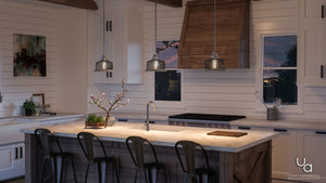 Modern kitchen with a marble island, four metal chairs, a UHP2730 Vintage Pendant Light from the Eugene Collection by Urban Ambiance in brushed nickel finish hanging overhead, a sink, plants, white cabinets, and a wooden range hood, illuminated by evening light streaming through the windows.