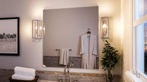 Modern bathroom with a large mirror, Urban Ambiance UHP2750 Luxe Industrial Electric Bath / Wall Light from the Messina Collection, wall lights, a robe on a hook, towel on rack, potted plant, stacked towels, and a window letting in natural light. Stainless steel bath fixtures throughout add a sleek finishing touch.
